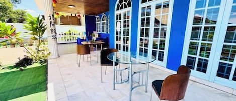 An outdoor patio with a glass table and chairs, surrounded by blue walls and large windows.