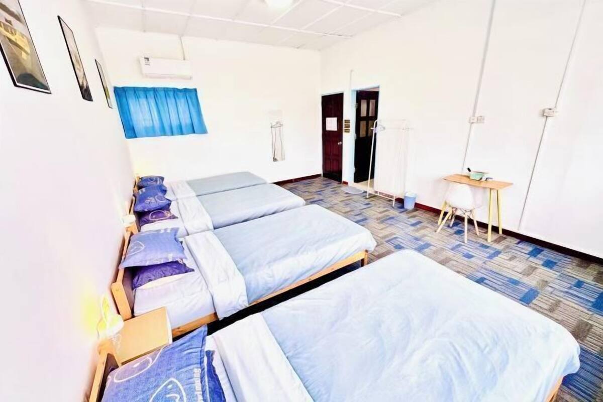A room with three single beds, a desk with a chair, and an air conditioning unit on the wall.