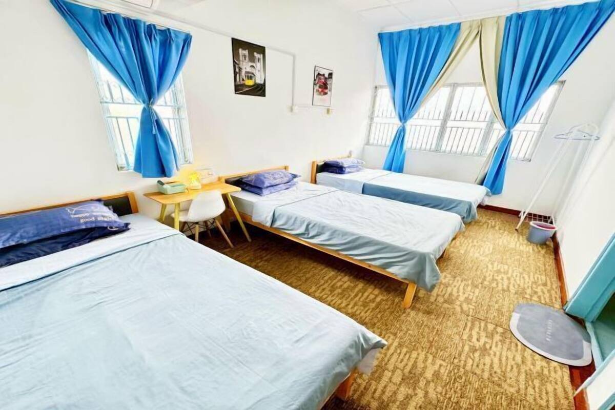 A dormitory room with three beds, a desk, and a chair.