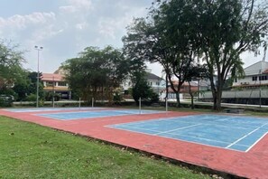 Un court de tennis en plein air, doté d’une surface rouge et bleue, entouré d’arbres et de bâtiments.
