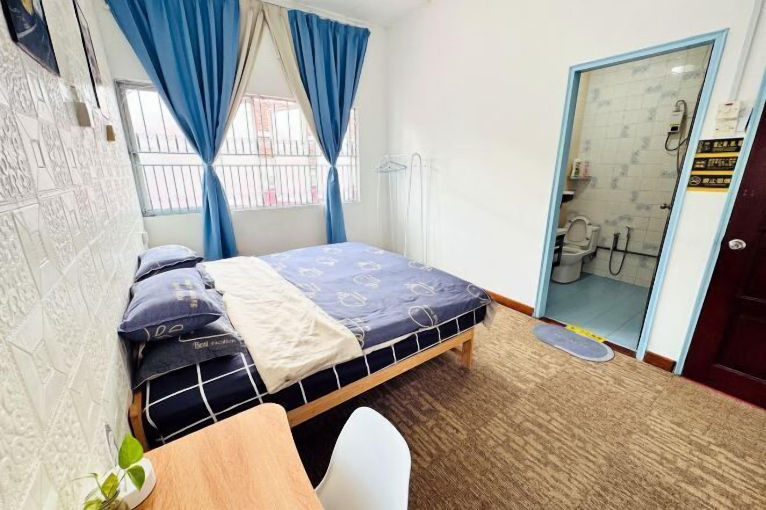 Een slaapkamer met een bed, een bureau, een stoel, een plant en een badkamer zichtbaar door een open deur.