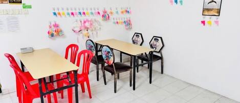 A classroom with tables and chairs, educational posters, and a large red poster on the wall.