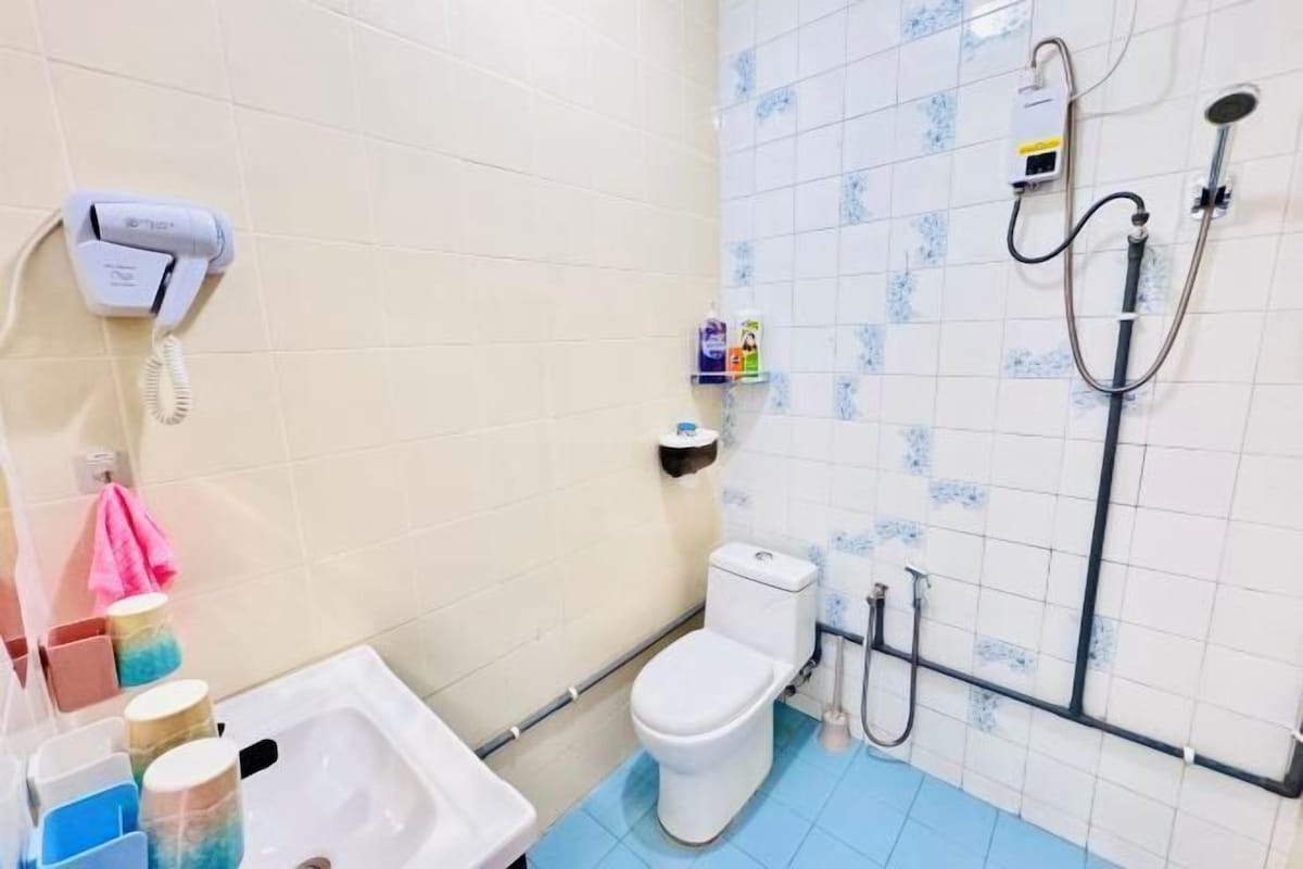 A bathroom with a toilet, a sink, a hairdryer, a shower, and a towel rack.