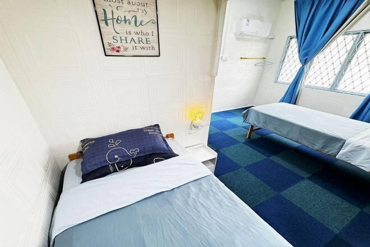 A room with two beds, a wall-mounted air conditioning unit, and a window with blue curtains.