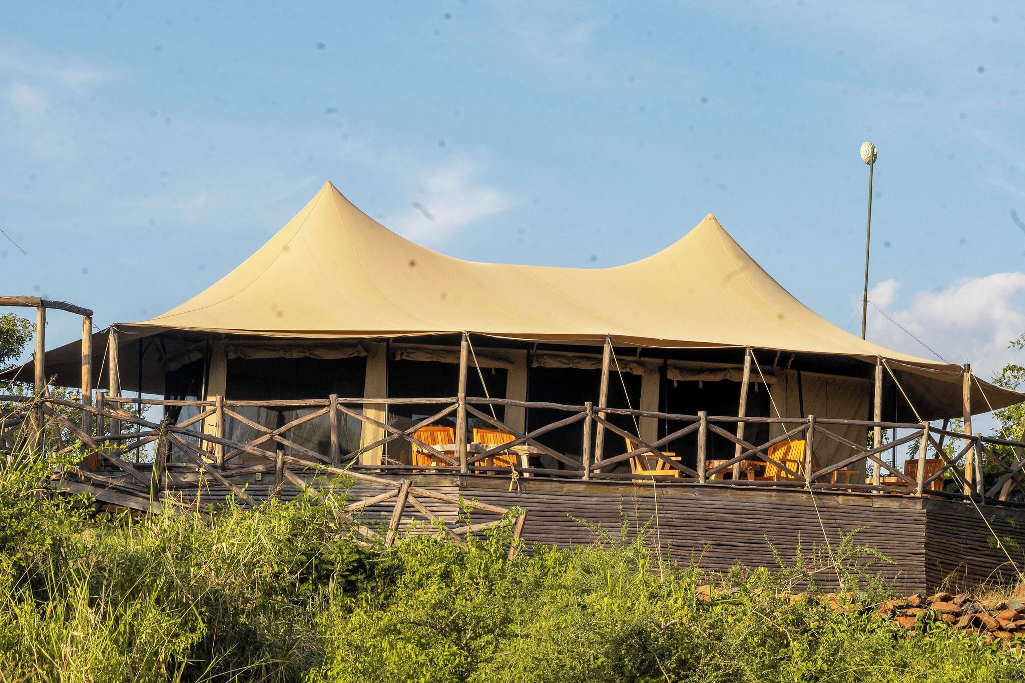 A safari tent with a wooden frame and a beige canopy, surrounded by greenery.