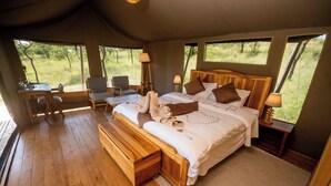 A tented room with a large bed, two chairs, a table, and a lamp. - Seregenti Kifaru Tented Lodge (Serengeti)