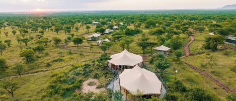 An aerial view of a safari lodge with multiple tents and a central structure with a peaked roof.