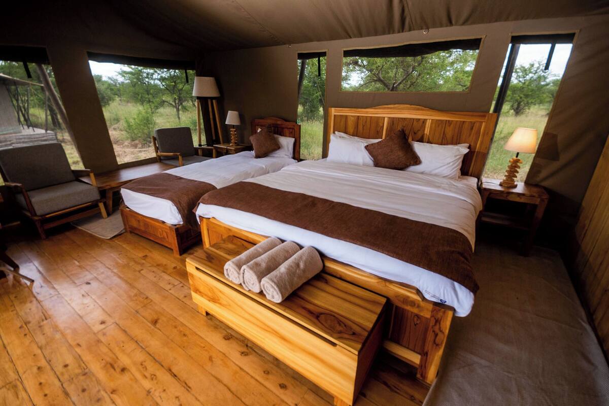 A double room with two beds, wooden furniture, and large windows offering a view of the outdoors.
