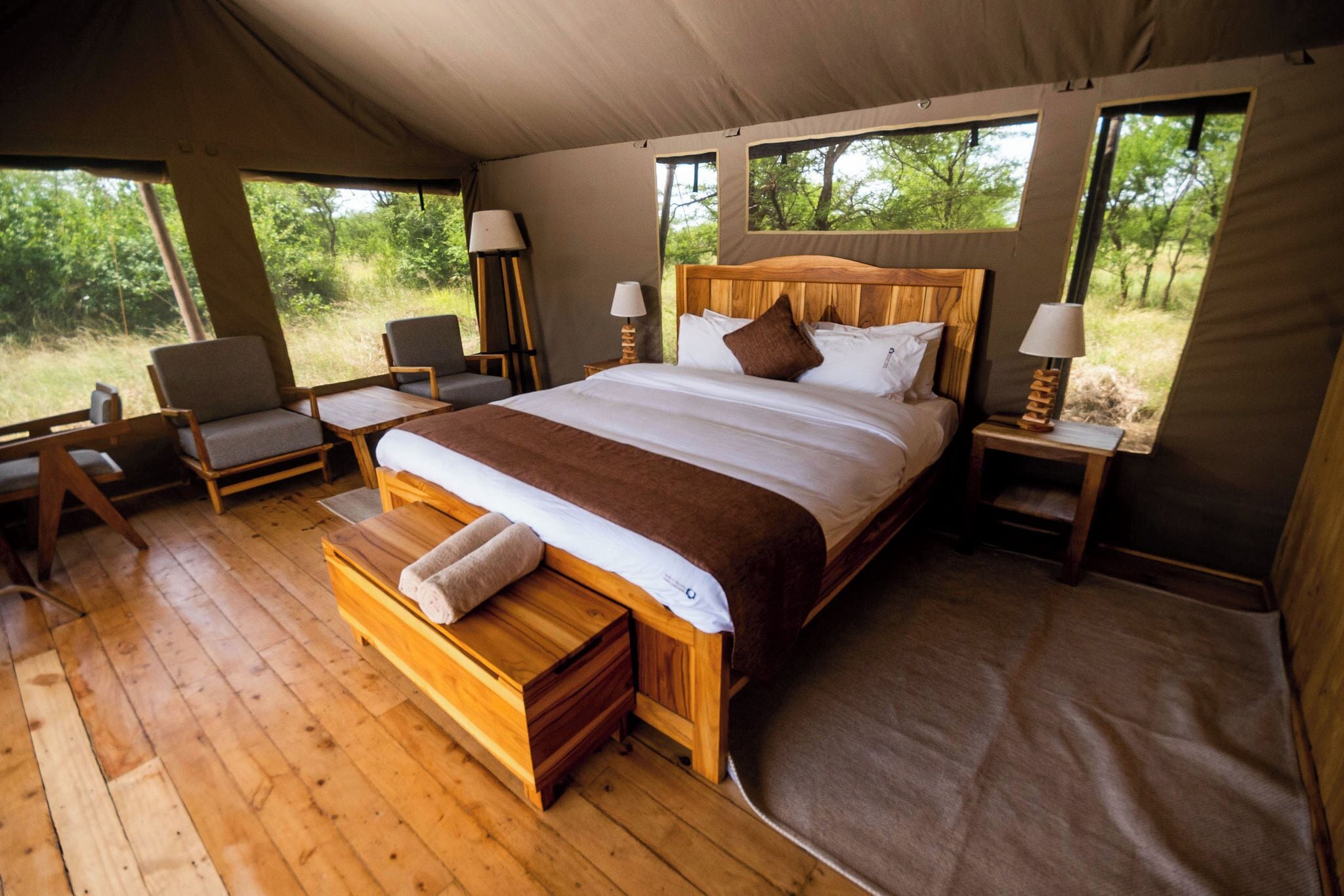 Een ruime tent met een groot bed, houten meubilair en uitzicht op de natuur.