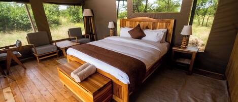 Een ruime tent met een groot bed, houten meubilair en uitzicht op de natuur.