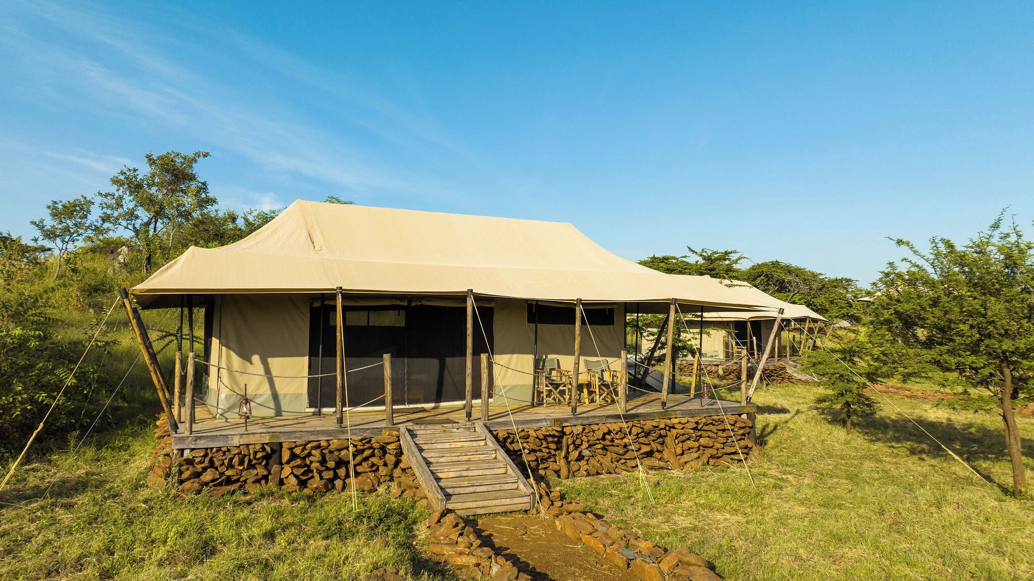 A safari tent with a covered porch and a stone foundation.