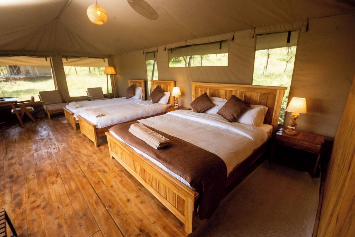 A tented accommodation with two wooden beds, each with a pillow and a bedside lamp.