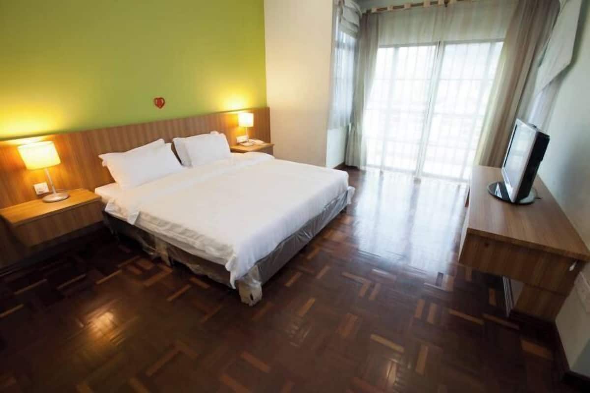 A hotel room with a bed, two bedside lamps, a TV on a wooden table, and a window with curtains.