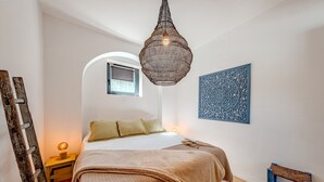 A bedroom with a bed, a hanging light fixture, a small window, and a decorative wall piece.