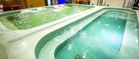 A large indoor swimming pool with multiple lanes, surrounded by a tiled floor and walls.
