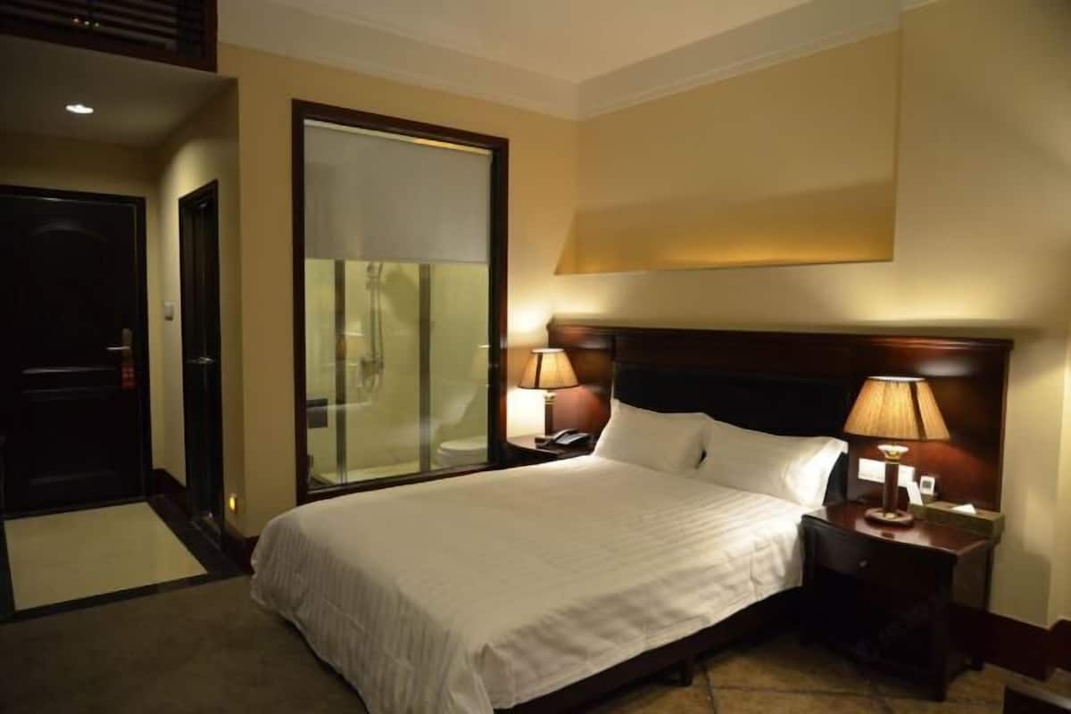 Een hotelkamer met een bed, twee bedlampen, een nachtkastje, een glazen deur naar een badkamer en een tapijtvloer.