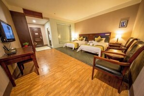 Habitación de hotel con dos camas, un escritorio, televisor y zona de estar.