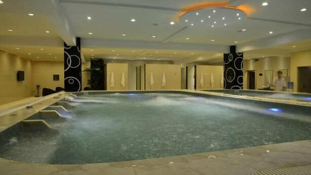 A large indoor swimming pool with multiple lanes, surrounded by walls with circular patterns, and a ceiling with recessed lighting. - Huangguang Holiday Hotel (Kaiping)