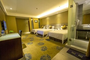 A hotel room with two beds, a desk, a shower area, and a television.