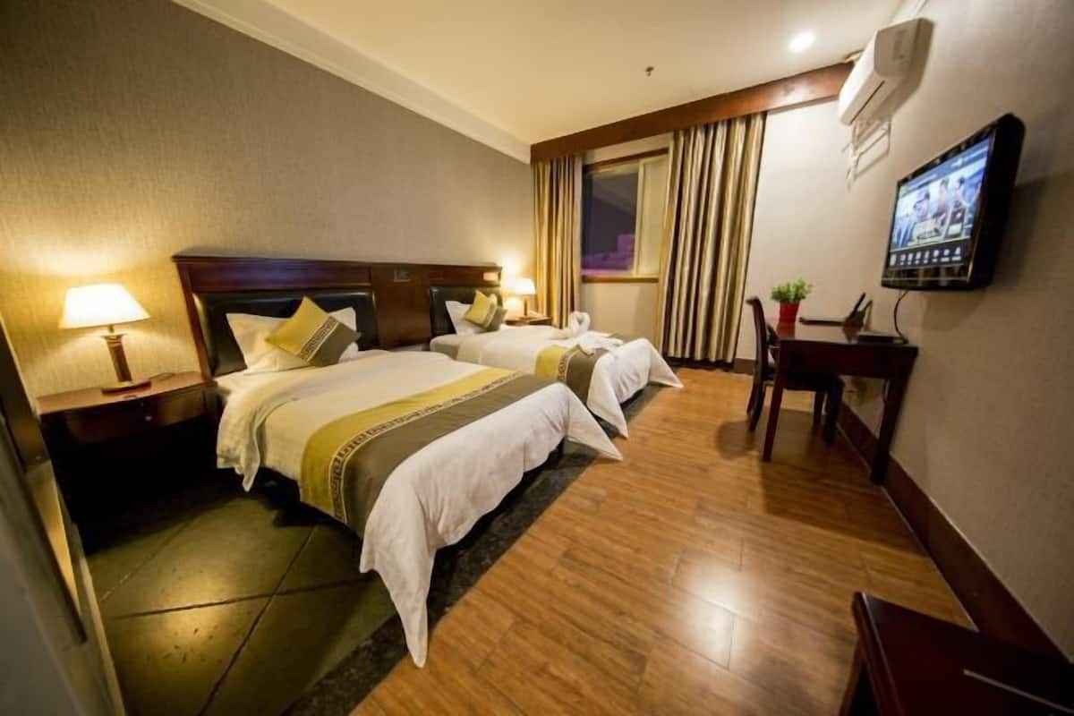 Een hotelkamer met twee bedden, een televisie, een bureau en een raam met gordijnen.