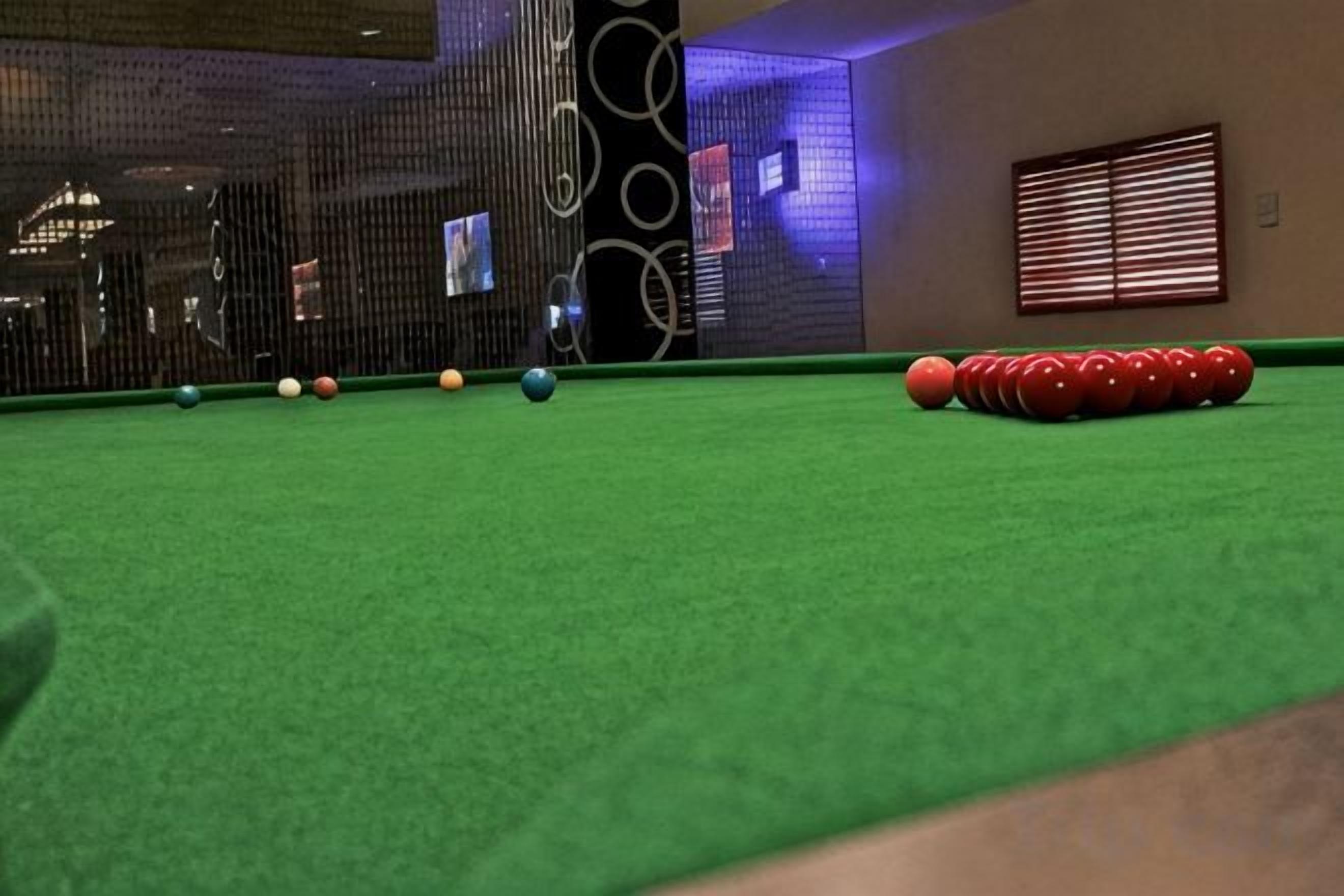 A pool table with balls arranged in a line, a wall with circular patterns, and a window with blinds.