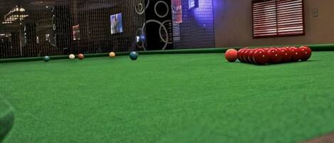A pool table with balls arranged in a line, a wall with circular patterns, and a window with blinds.