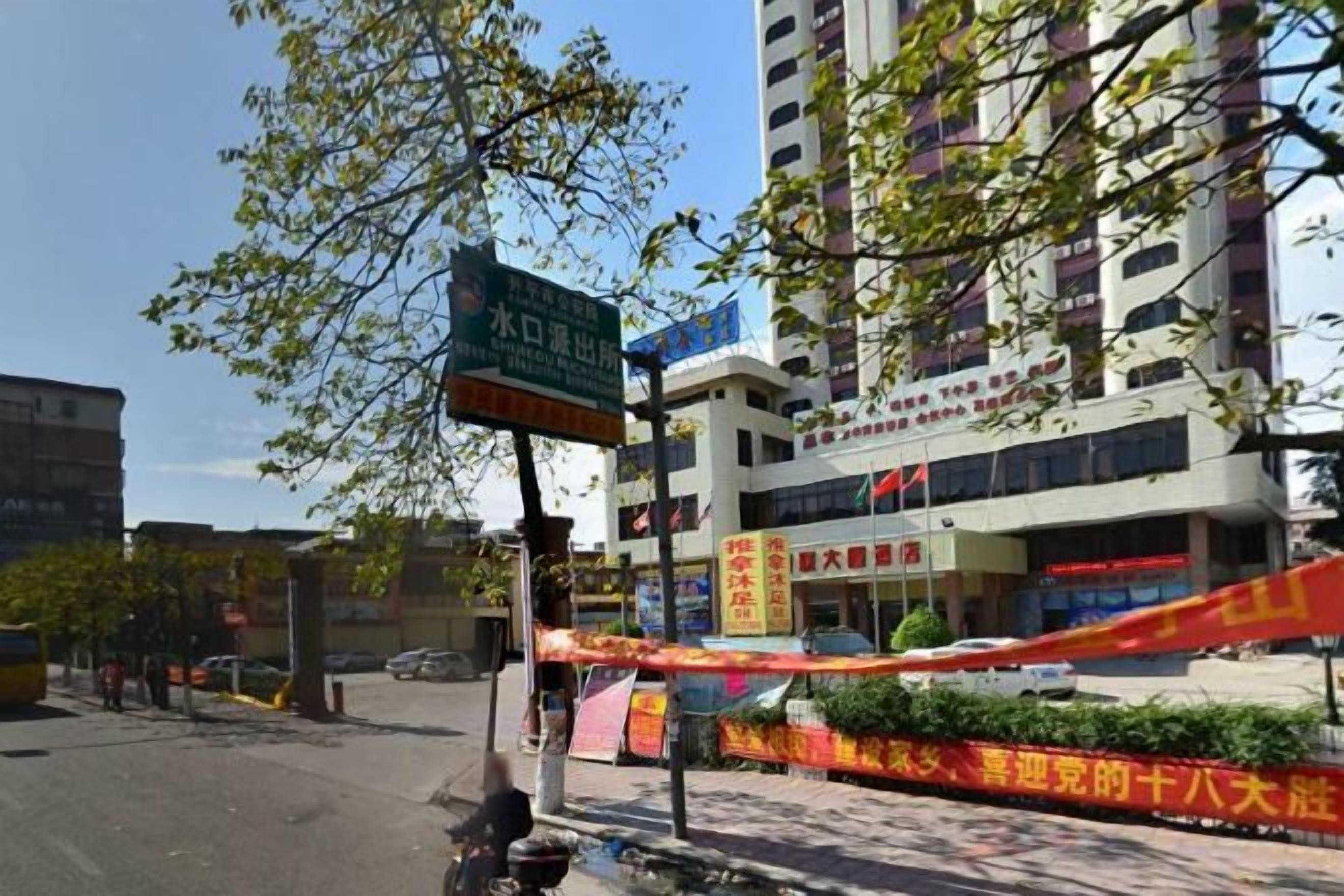 A hotel with a signboard, a multi-story building, and a street in front.