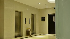 A hallway with three elevators, a trash bin, and a door. - Huangguang Holiday Hotel (Kaiping)