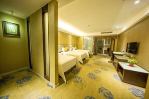 A hotel room with two beds, a desk, a television, and a bathroom with a glass door.