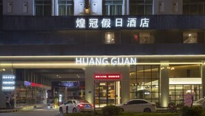A hotel entrance with illuminated signage, a car parked in front, and a pedestrian walkway. - Huangguang Holiday Hotel (Kaiping)