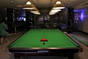 A pool table with balls, a person walking, and a wall with circular patterns. - Huangguang Holiday Hotel (Kaiping)