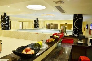 Un vestíbulo de hotel con una recepción, una piscina interior amplia y una máquina de café.
