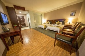 Habitación de hotel con dos camas, un escritorio, televisor y zona de estar.
