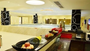 A hotel lobby with a large indoor pool, a reception desk, and a fruit bowl on the counter. - Huangguang Holiday Hotel (Kaiping)