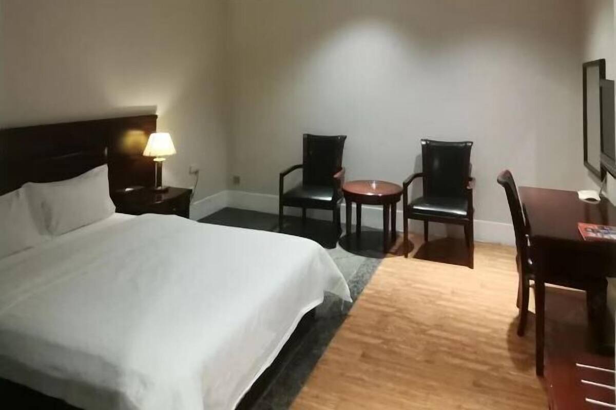 Een hotelkamer met een bed, een bureau, twee stoelen, een lamp en een televisie.