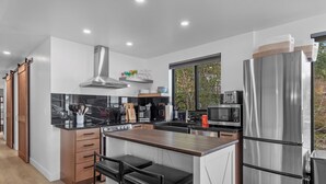 A modern kitchen with a central island, stainless steel appliances, and a view of the outdoors through a large window. - Lakefront Home with Private Beach and Dock | Outdoor Dining (Harrison)
