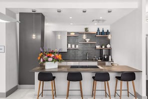 Una cucina moderna con isola centrale, sgabelli da bar e scaffali a scomparsa.