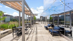 En udendørs terrasse med borde og stole, lyskæder og et skilt med 'NO GLASS ALLOWED'.