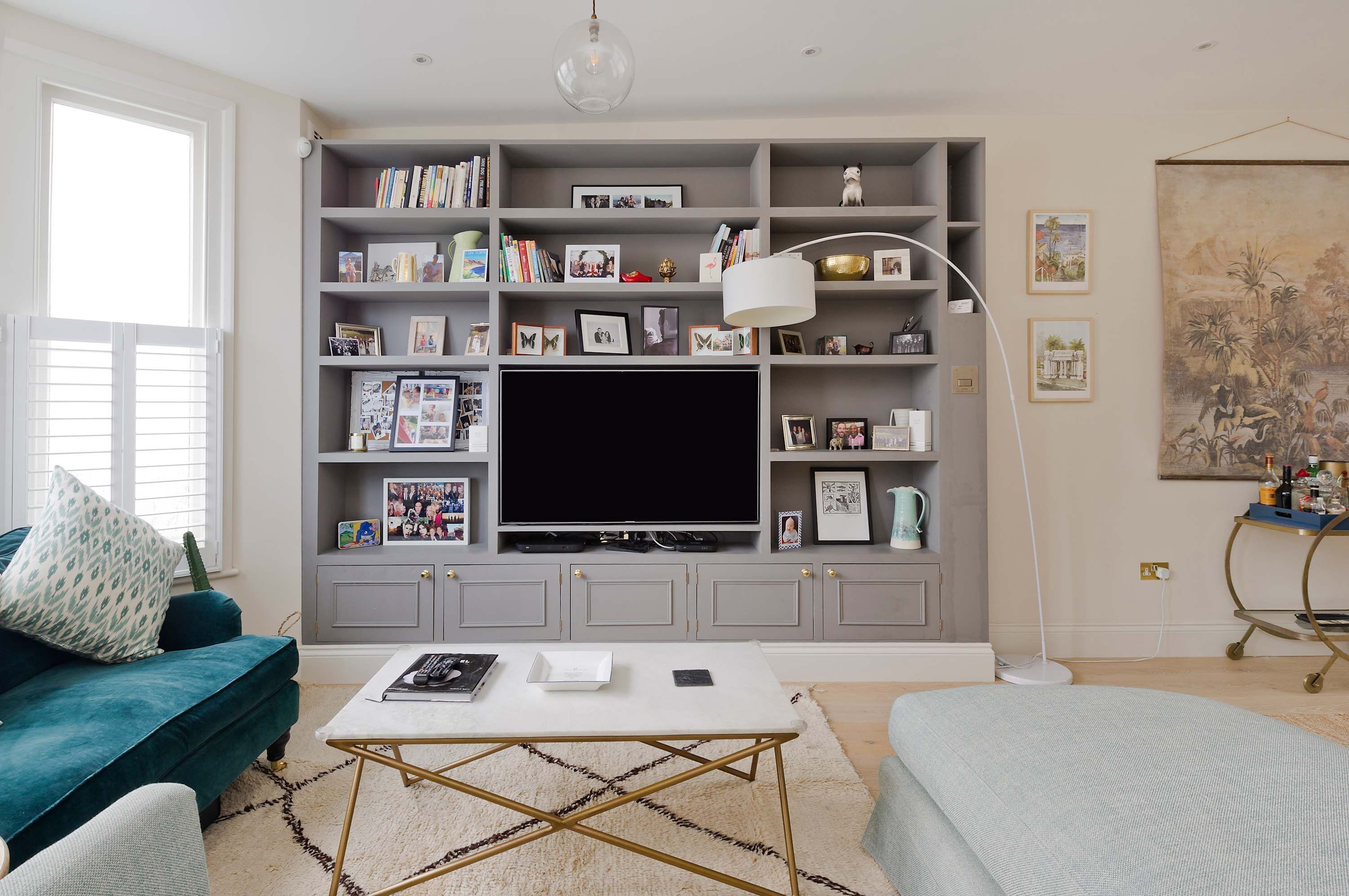 A living room with a grey entertainment unit, a flat-screen TV, a white coffee table, and a teal sofa.