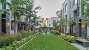 A modern residential building with a central courtyard, featuring a well-maintained lawn, outdoor seating, and a small play area. - Private Bedroom With Bathroom Central Location (Santa Ana)
