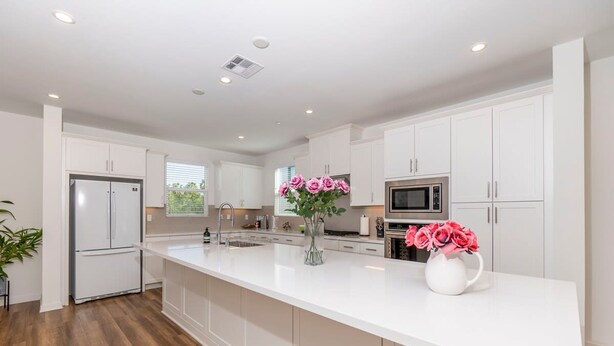 A modern kitchen with white cabinetry, a large island, stainless steel appliances, and decorative pink roses. - Private Bedroom With Bathroom Central Location (Santa Ana)