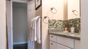 Un baño con salpicadero de azulejos, una encimera con artículos de aseo y un perchero con toallas.