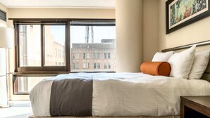Una habitación de hotel con una cama grande, una ventana que ofrece vistas a edificios y un cuadro en la pared.