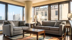 Una habitación de hotel moderna con dos sofás, una mesa de centro y vistas de la ciudad a través de amplias ventanas.
