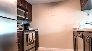 Una cocina con electrodomésticos de acero inoxidable, incluyendo un refrigerador, horno y microondas. Hay una encimera con una cafetera y un lavamanos.