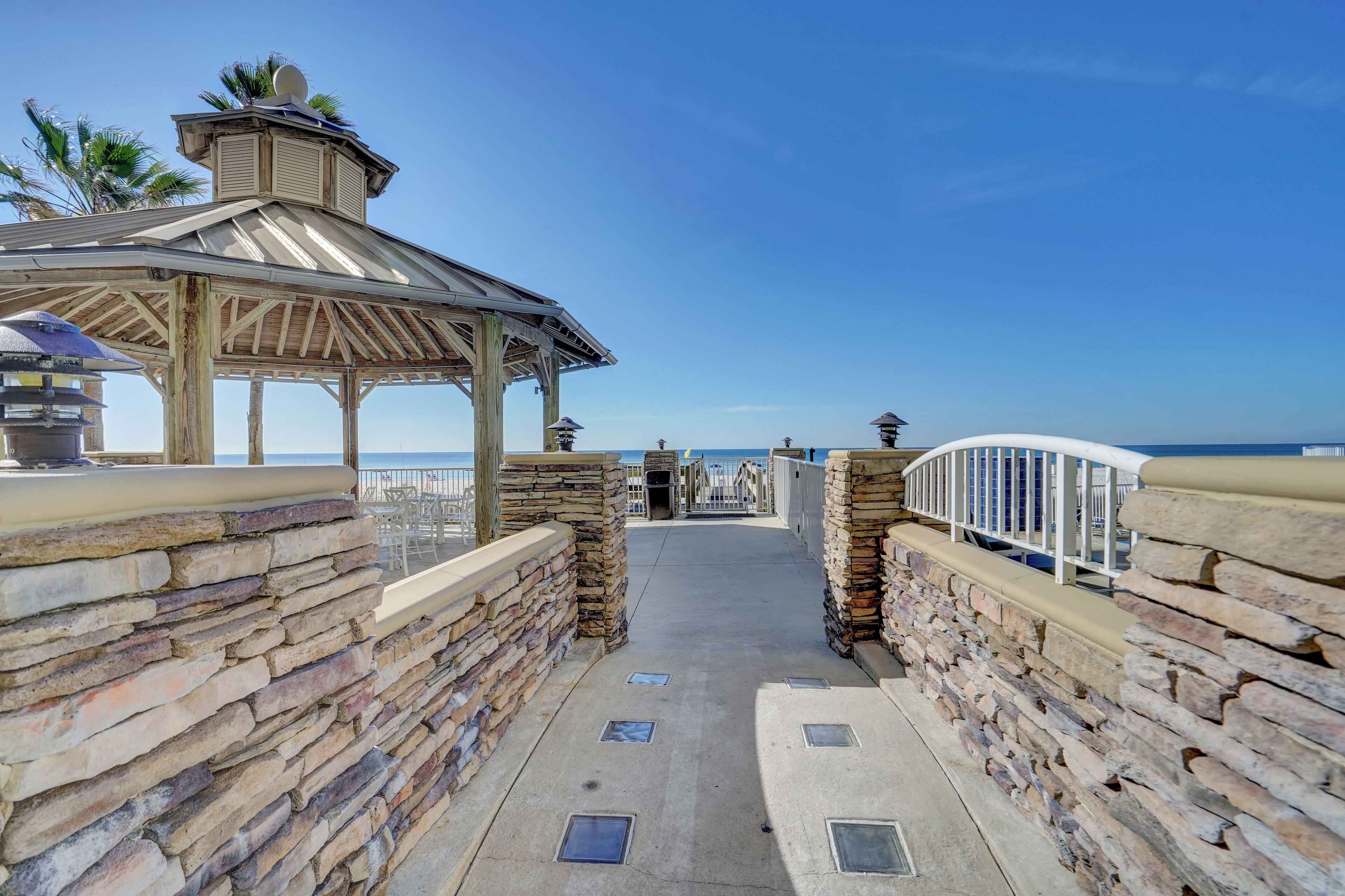 A stone pathway leading to a beach with a gazebo and a view of the ocean.