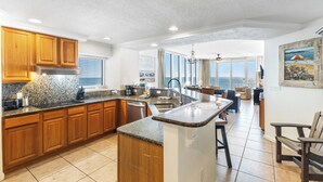 A spacious kitchen with granite countertops, wooden cabinets, and a large island. It features a view of the ocean through large windows and a dining area with a view.