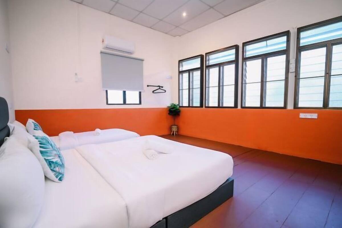 A hotel room with two beds, an air conditioning unit, a window with blinds, and a small plant.