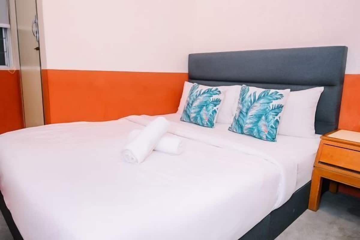 A neatly made bed with white linens and two decorative pillows, a wooden nightstand beside it, and a grey headboard.