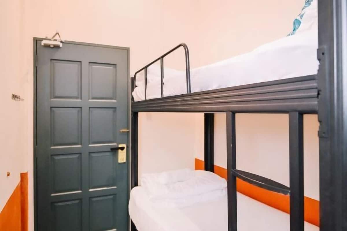 A bunk bed with a white mattress and orange trim, a closed door with a handle, and a small orange object on the floor.